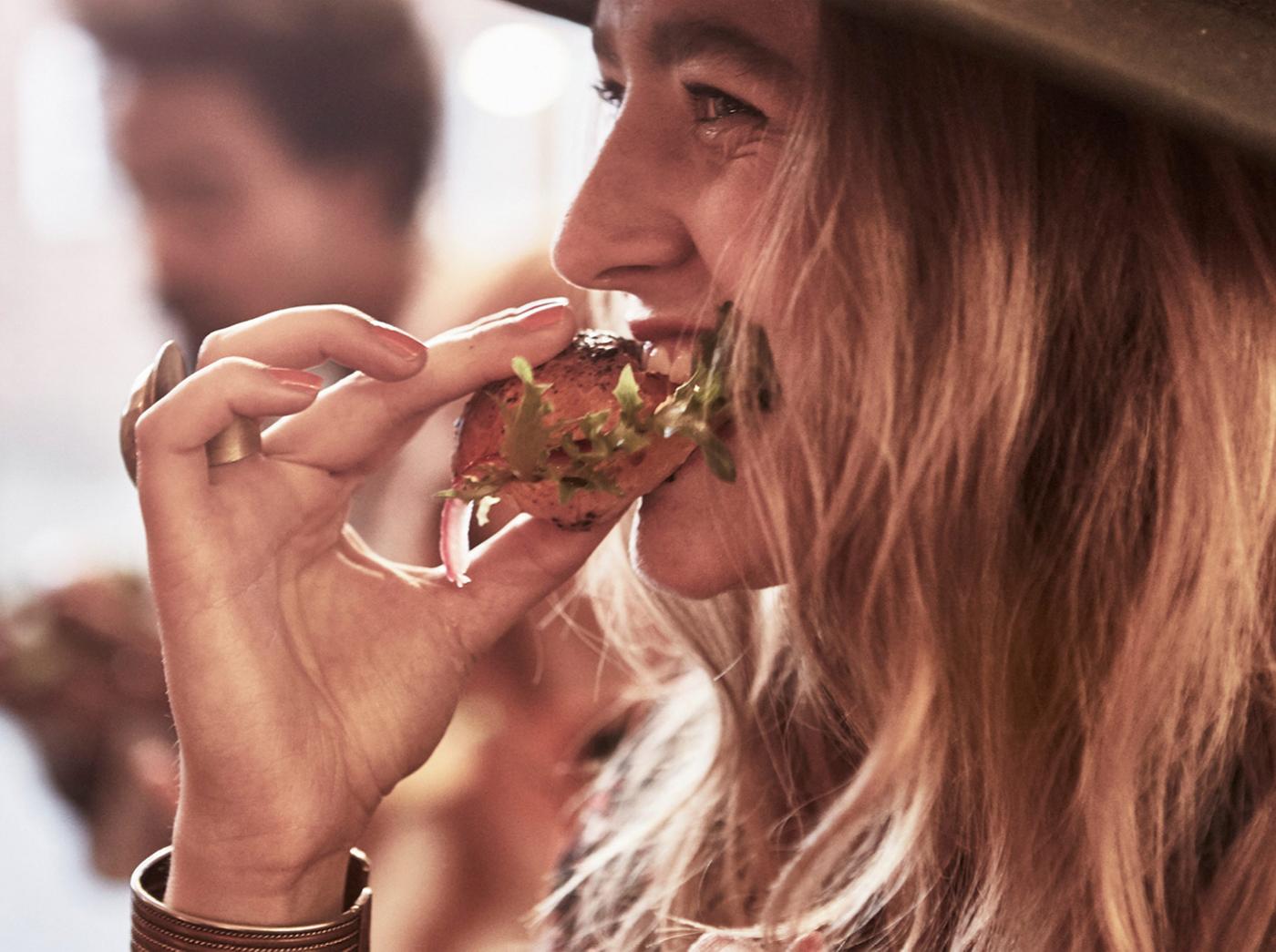 A girl eating a snack with bread and salad in it.