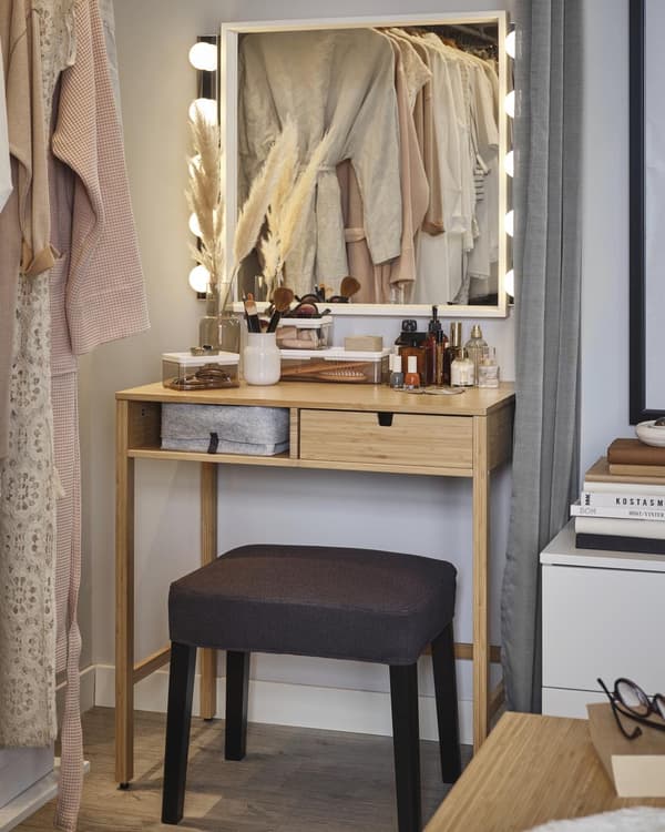 A girl looking into a mirror with lights above a white desk.