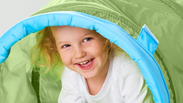A girl peeks out of a green play tunnel, laughing