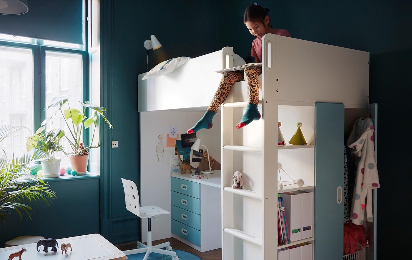 A girl sitting on a bunk bed with study area underneath.