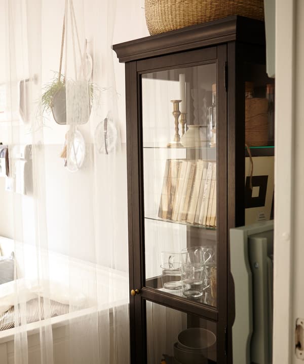 A glass cabinet in a kitchen filled with books, glassware, and other collectables.