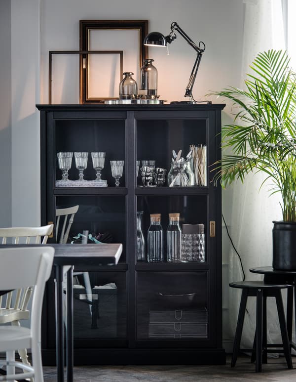 A glass-door cabinet holds glasses, plates, and decorative pieces in a white dining room.