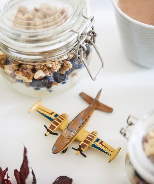 A glass jar filled with granola, plus a toy plane on a white surface.