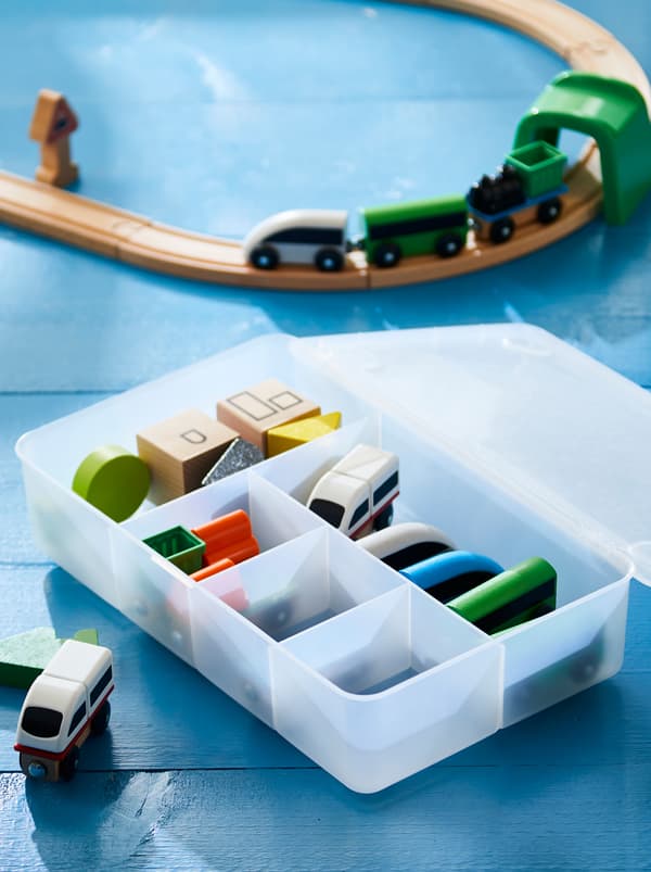 A GLIS box filled with sorted accessories, beside a wooden train on a track.