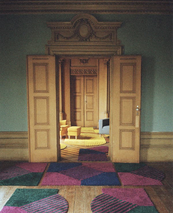 A grand doorway with patterned rugs in front, opening up to a living room with yellow chair, footstool and rugs.