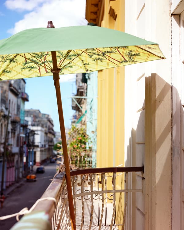 A green and yellow printed parasol leaning against a railing on a balcony above a street.