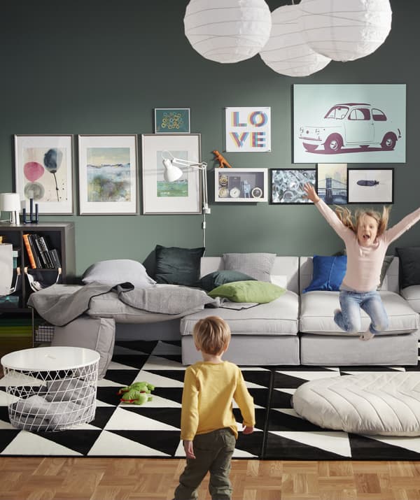 A green living room with large grey modular sofa and two kids playing.