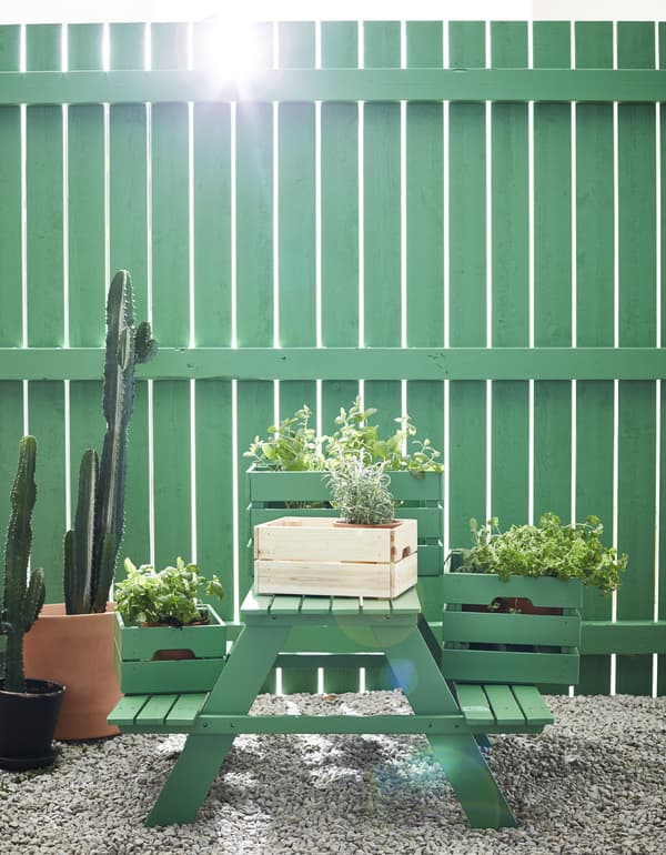 A green picnic bench with crates of plants on top.