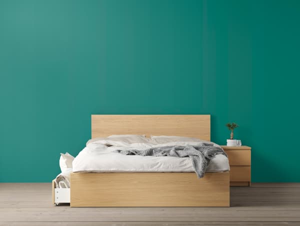A green wall with a natural wood bed frame and white bedlinen