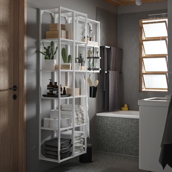 A grey bathroom with a large white shelving unit with a black swivel shelf. Plants, towels and boxes are on the shelves.