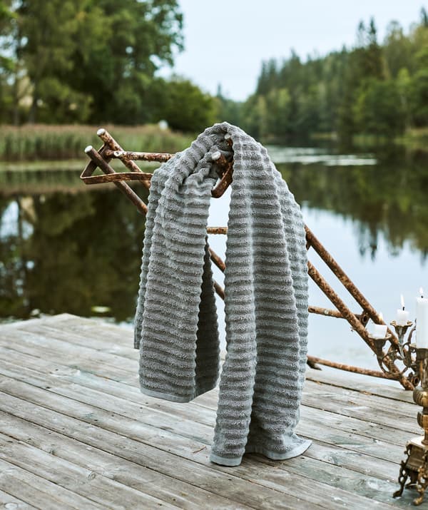 A grey fluffy towel hangs from a rusted set of steps that lead from a decked area beside a lake down to the water.