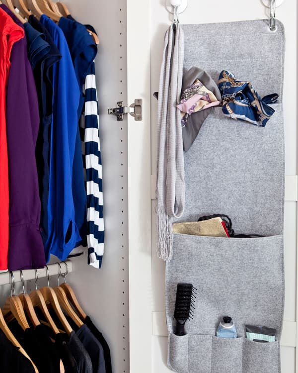 A grey hanging organiser on the inside of a wardrobe door. Clothes hang on two rails in the wardrobe.