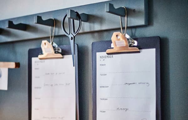 A grey hook rack with two black clip boards hanging from it 