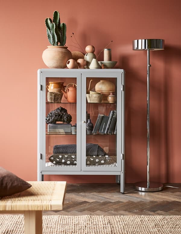 A grey IKEA FABRIKÖR glass-door cabinet displays decorative items in a living room.