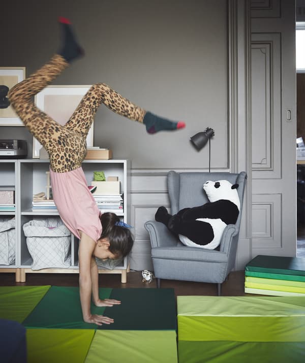 A grey living room with bright green play mats and a girl doing a handstand.