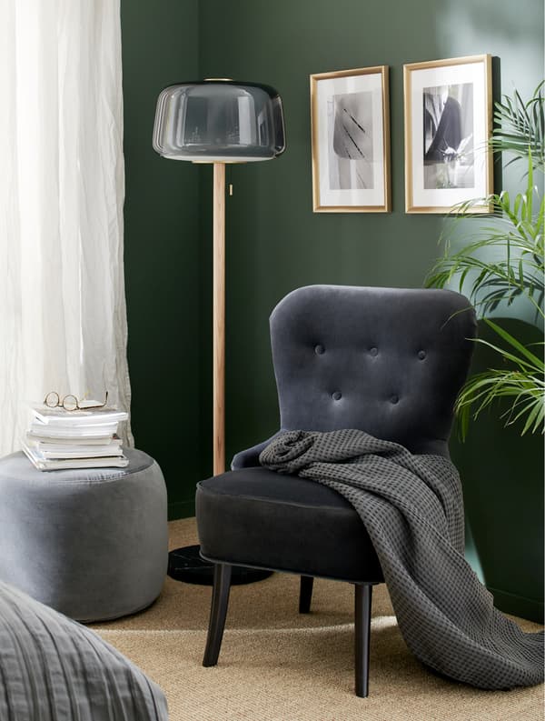 A grey velvet armchair, a grey floor lamp, a dark grey pouffe, a grey throw and gold-coloured frames.