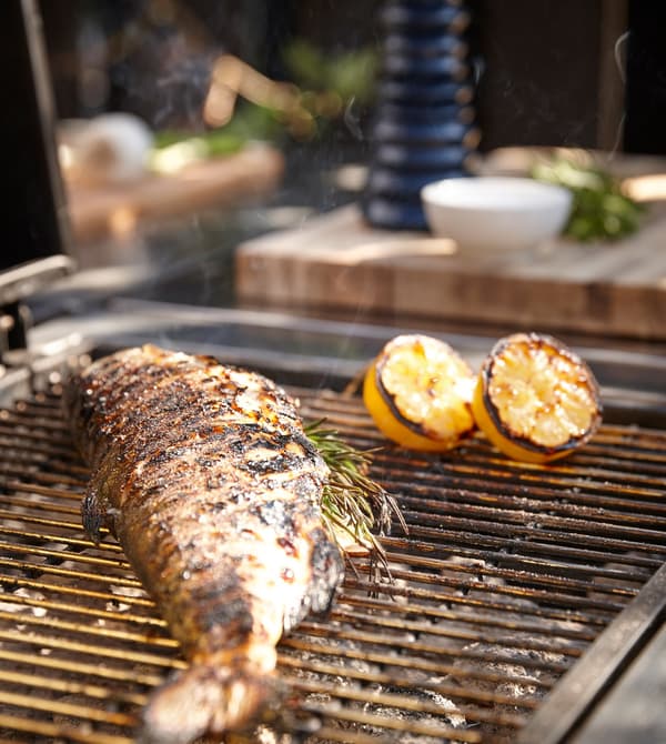 A grill with a whole fish and lemon halves cooking on top.