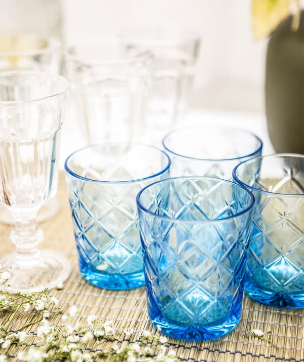 A group of blue cut glasses and clear wine glasses on a table runner.