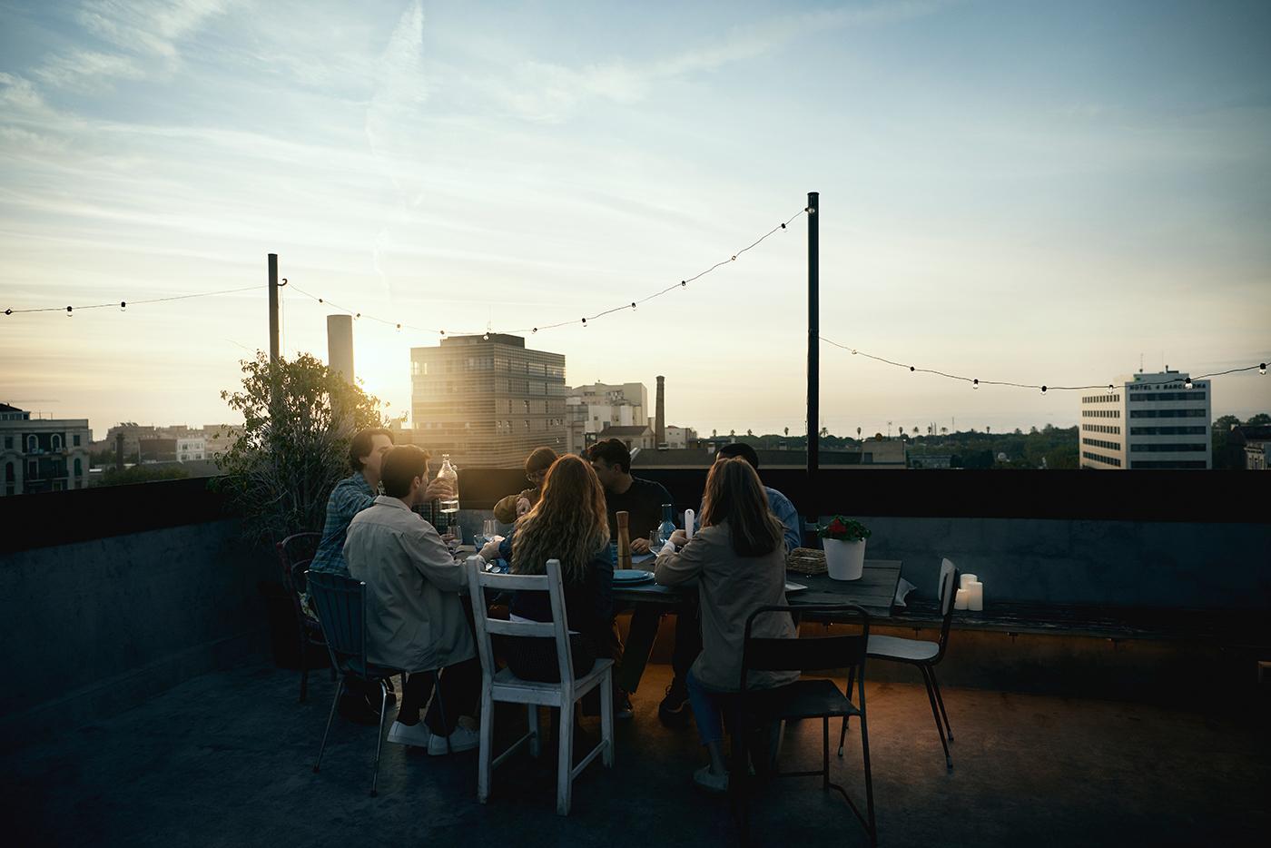 A group of friends gathered around a rooftop table at sunset.