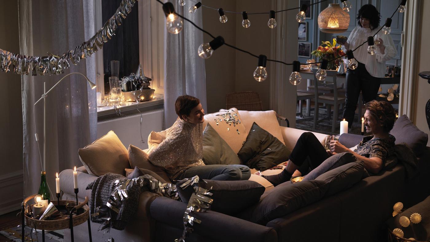 A group of friends gathered on a GRONLID sofa with LED string lights hanging on the ceiling.