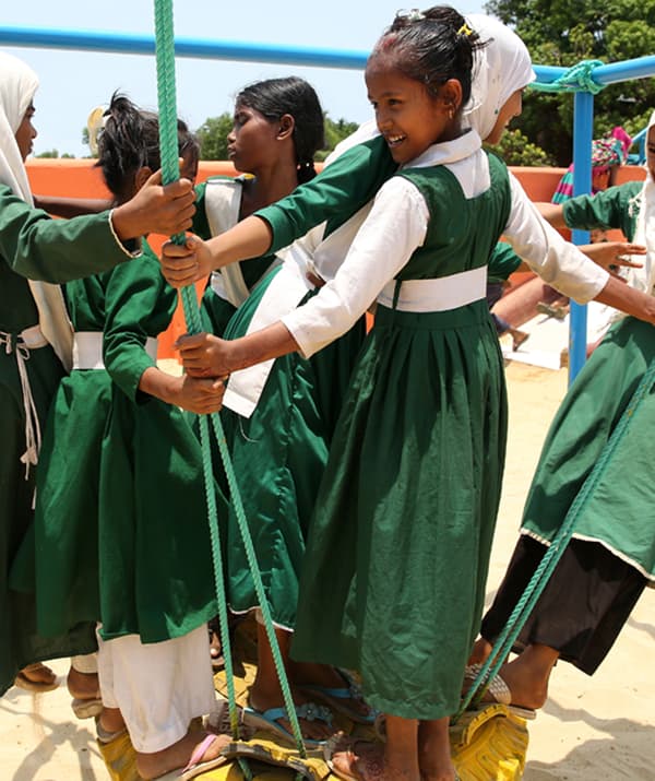 A group of girls in green dresses playing on a rope swing outdoors.