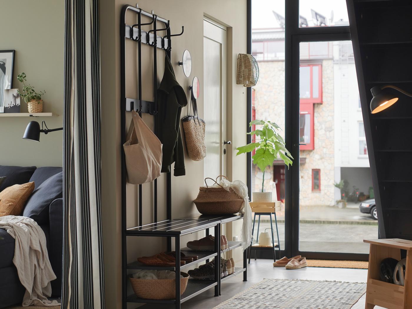 A hallway where a PINNIG coat rack with shoe storage bench stands against a wall holding a coat, baskets and shoes.