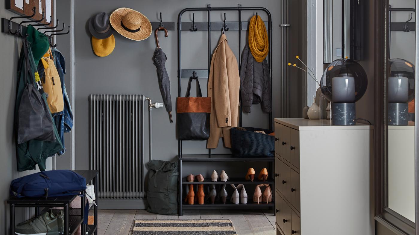 A hallway with a PINNIG coat rack, shoe bench and hook rack on two sides of the space holding coats, hats, bags and shoes.