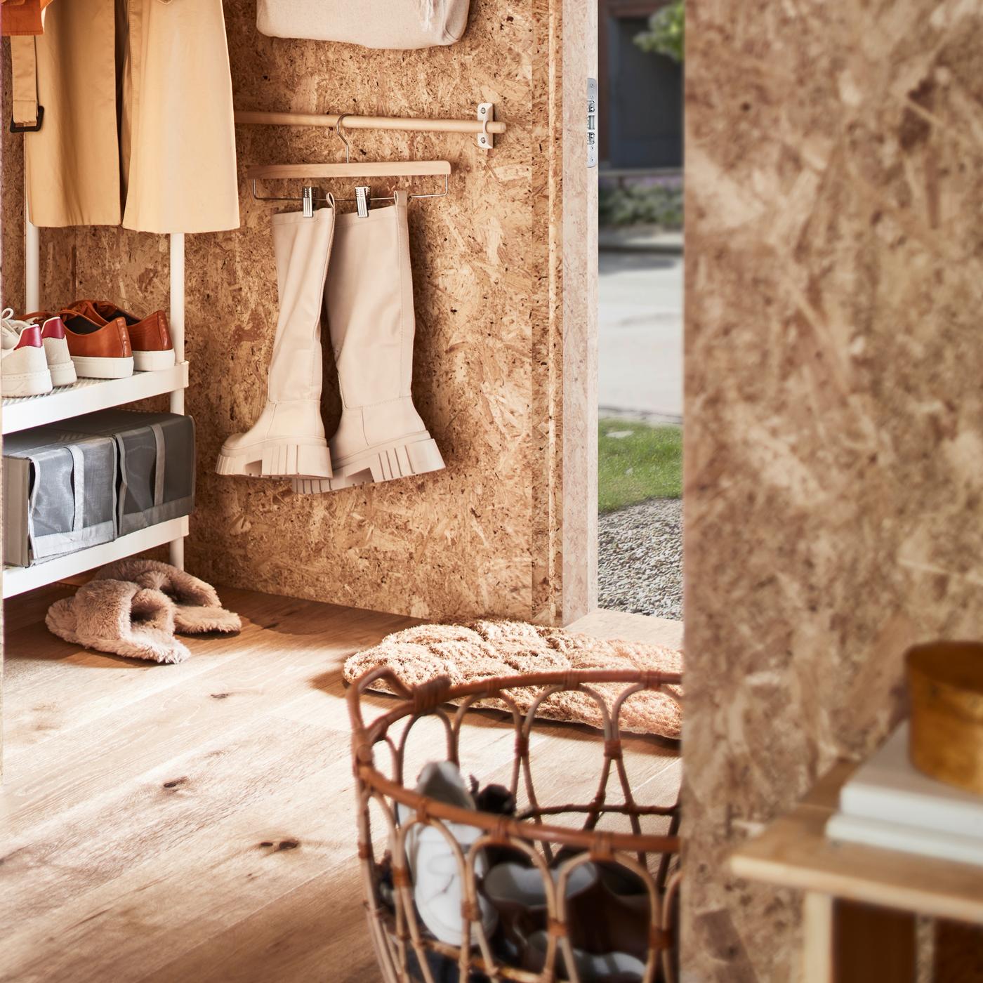 A hallway with a white coat rack with shoe storage, a rattan basket with shoes plus a rail with boots on a skirt hanger.