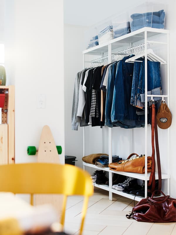 A hallway with a white MACKAPÄR coat rack with clothes, both on hangers and in boxes on a top shelf, shoes and accessories.