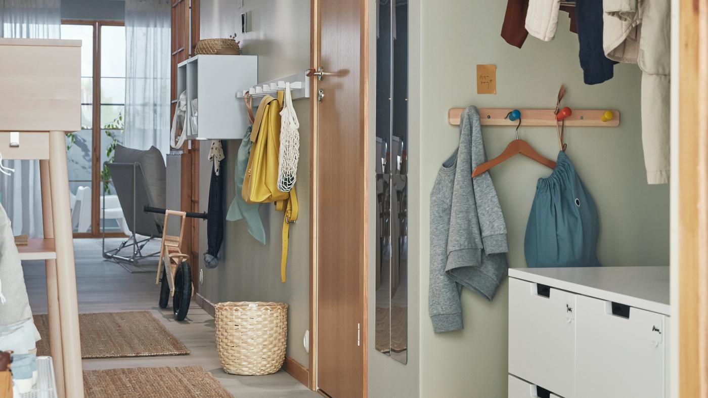 A hallway with rugs on the floor, a NORDLI chest of drawers, and FLISAT and KUBBIS hook racks and EKET shelving on the wall.