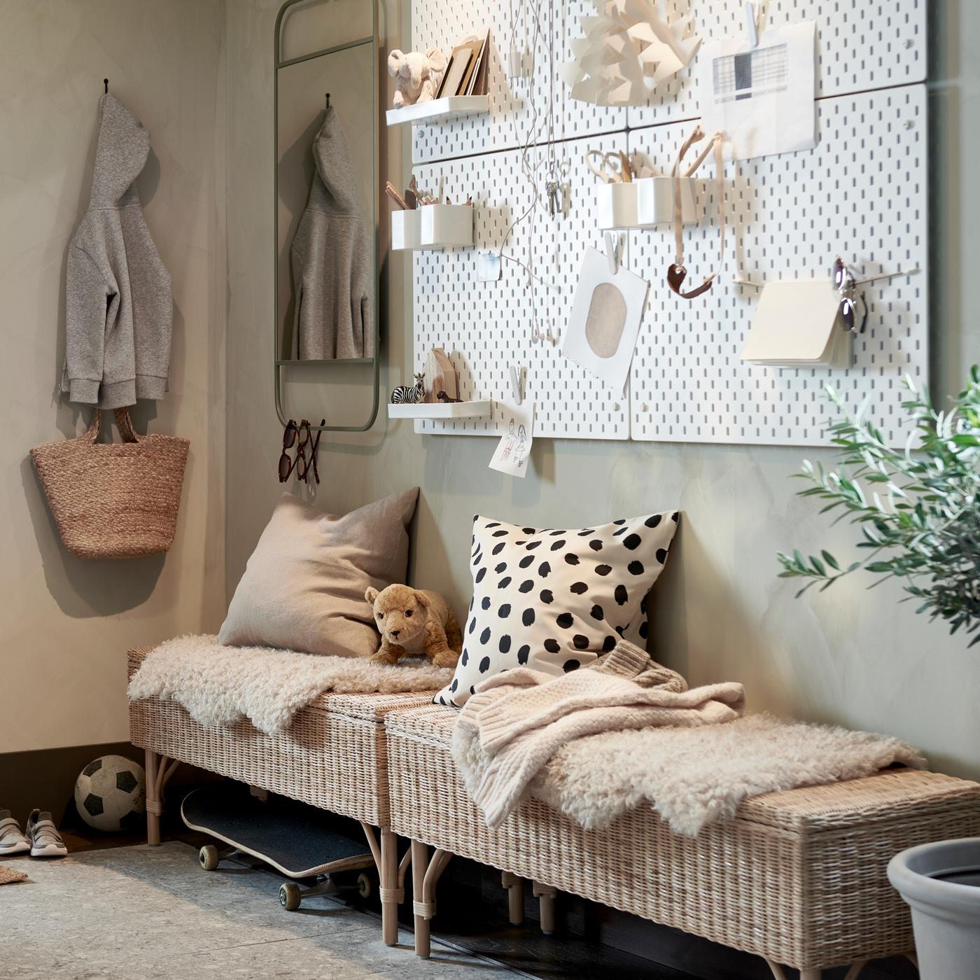 A hallway with two rattan benches with storage, a wall with white pegboards and a green mirror, plus a large potted plant.