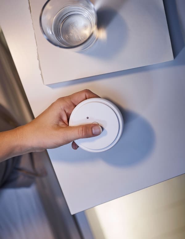 A hand holding a remote control, to adjust the lighting underneath a bedframe.
