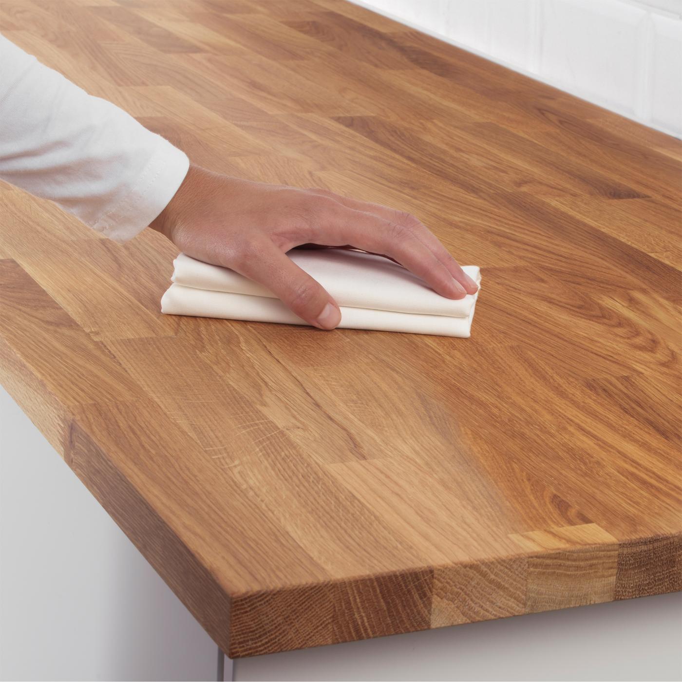 A hand holds a white cleaning cloth against the surface of a wooden kitchen worktop.