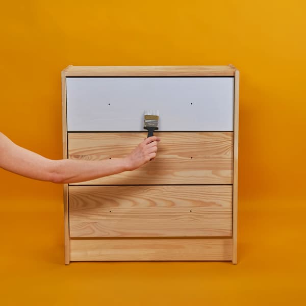 A hand is holding painting the drawer with white paint.