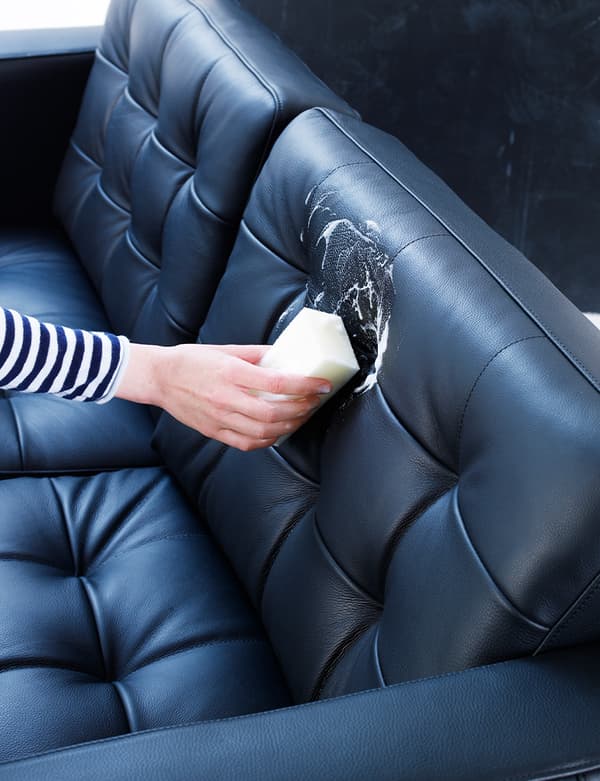 A hand is seen applying leather conditioner to a black leather couch.