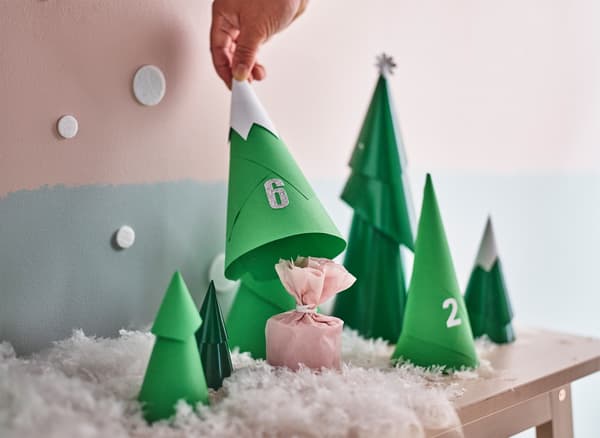 A hand lifting up a paper tree to show the wrapped present underneath that’s part of an advent calendar.