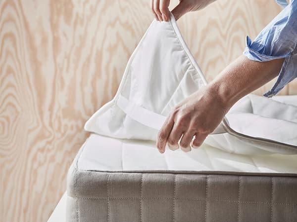 A hand peeling away a mattress protector from the corner of a mattress with a wooden background.