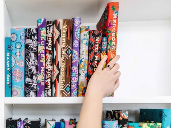 A hand placing books wrapped in fabric with names printed in gold on each book spine onto a bookcase.