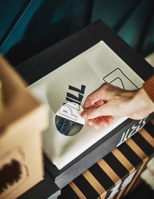 A hand pulling back a piece of paper covering a hole on a wrapped box.