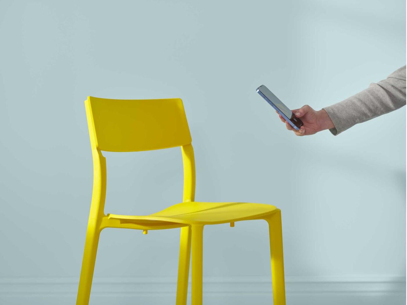 A hand reaches out to take a phone picture of a yellow IKEA chair.