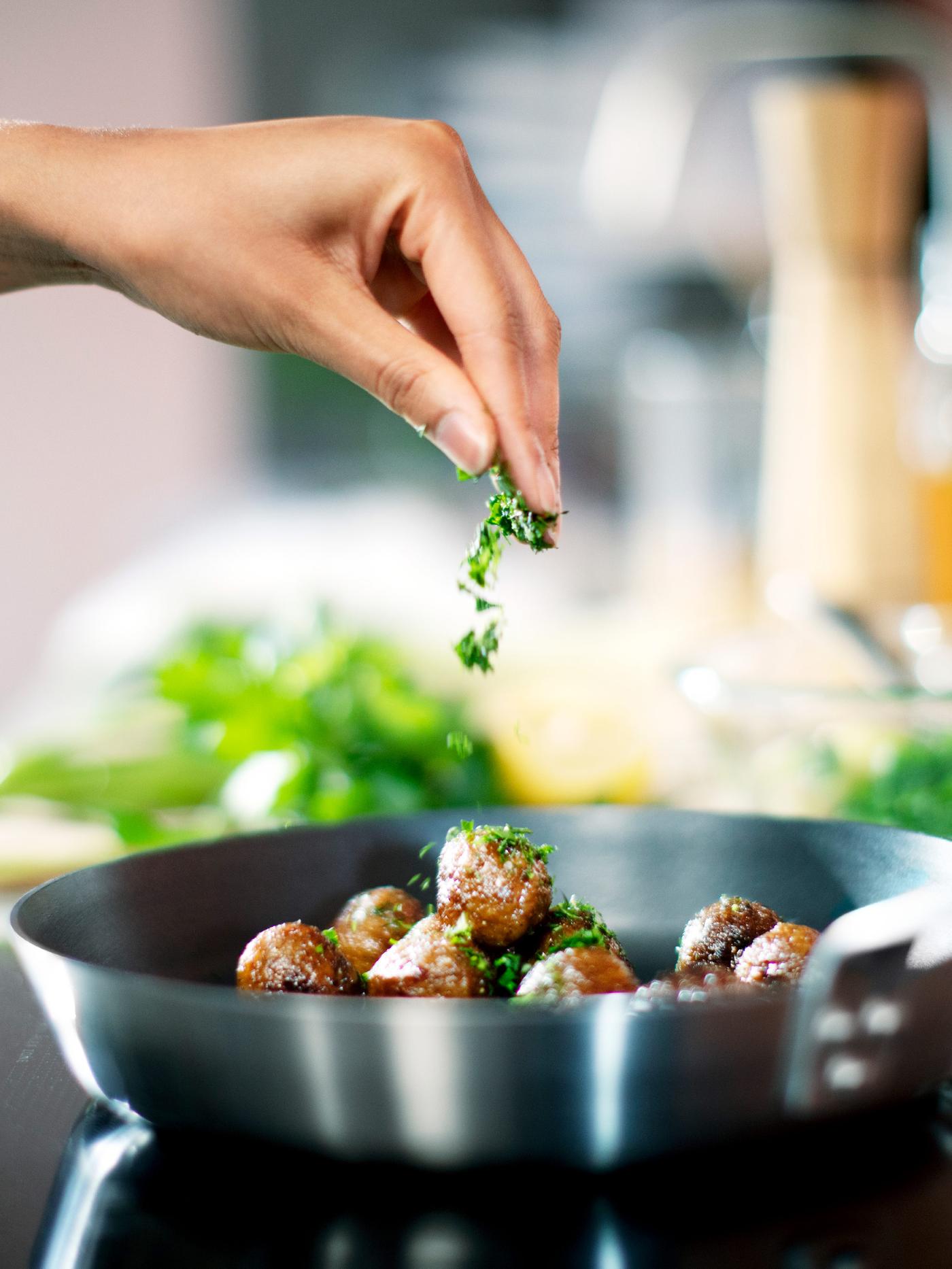 A hand seasoning HUVUDROLL plant balls in an IKEA 365+ frying pan.