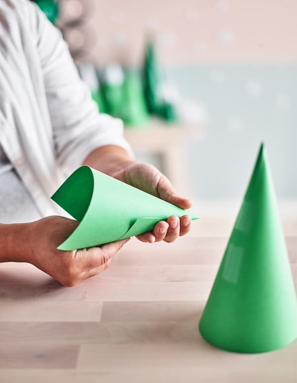 A hand twisting paper into a cone shape to make advent calendar trees.