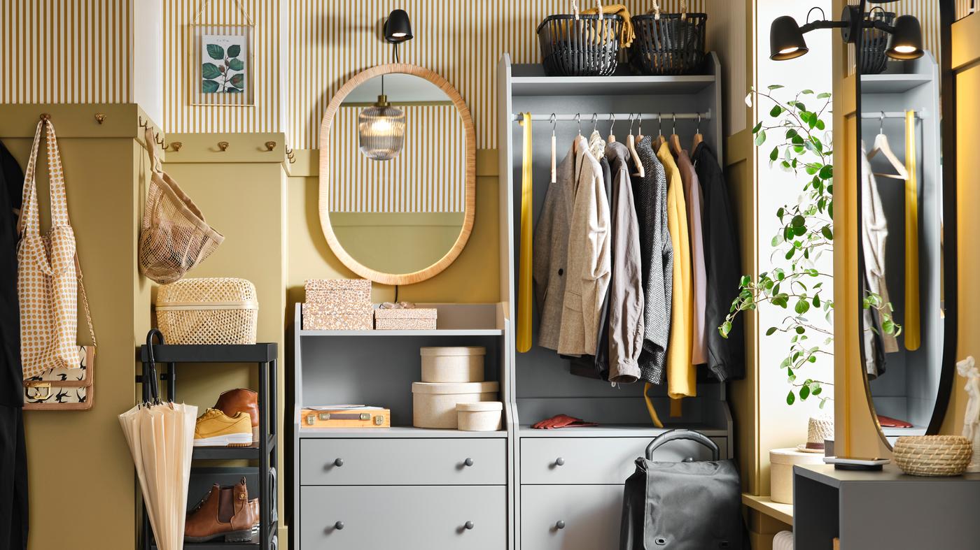 A HAUGA chest of drawers and a HAUGA open wardrobe holding clothes, boxes and baskets stand in a small hallway.