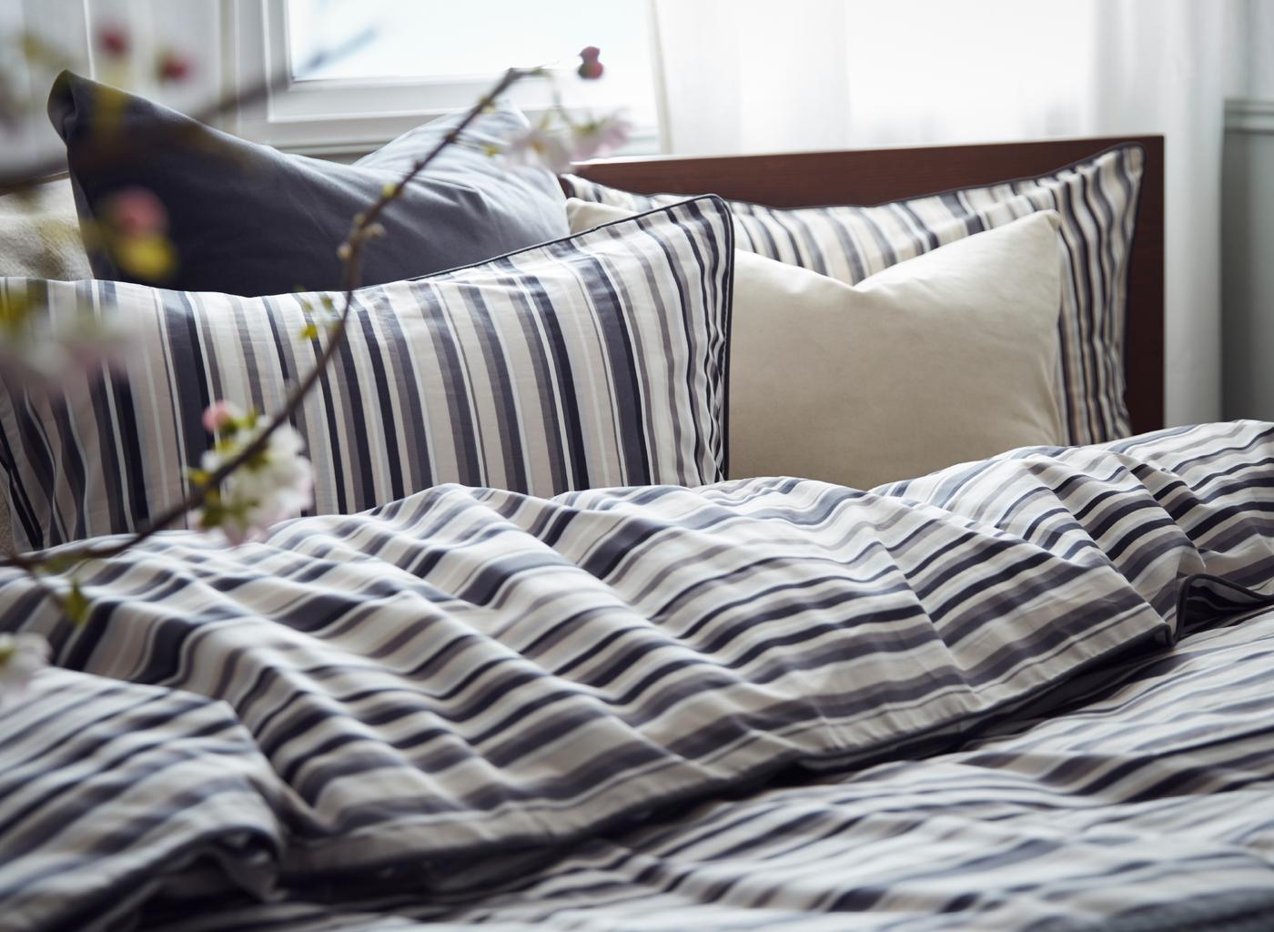 A headboard with RANDGRÄS cotton bed linen with pillows and a quilt cover in shades of white and grey, some striped.
