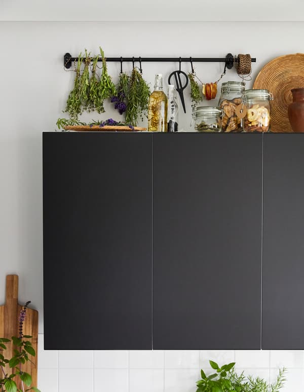 A herb drying rack created from a black FINTORP rail above black kitchen wall units.