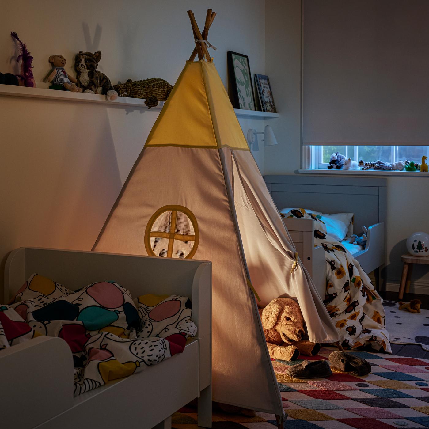 A HÖVLIG children’s tent on a multicolour BUSENKEL rug between two white extendable beds. Picture ledges are on the wall.