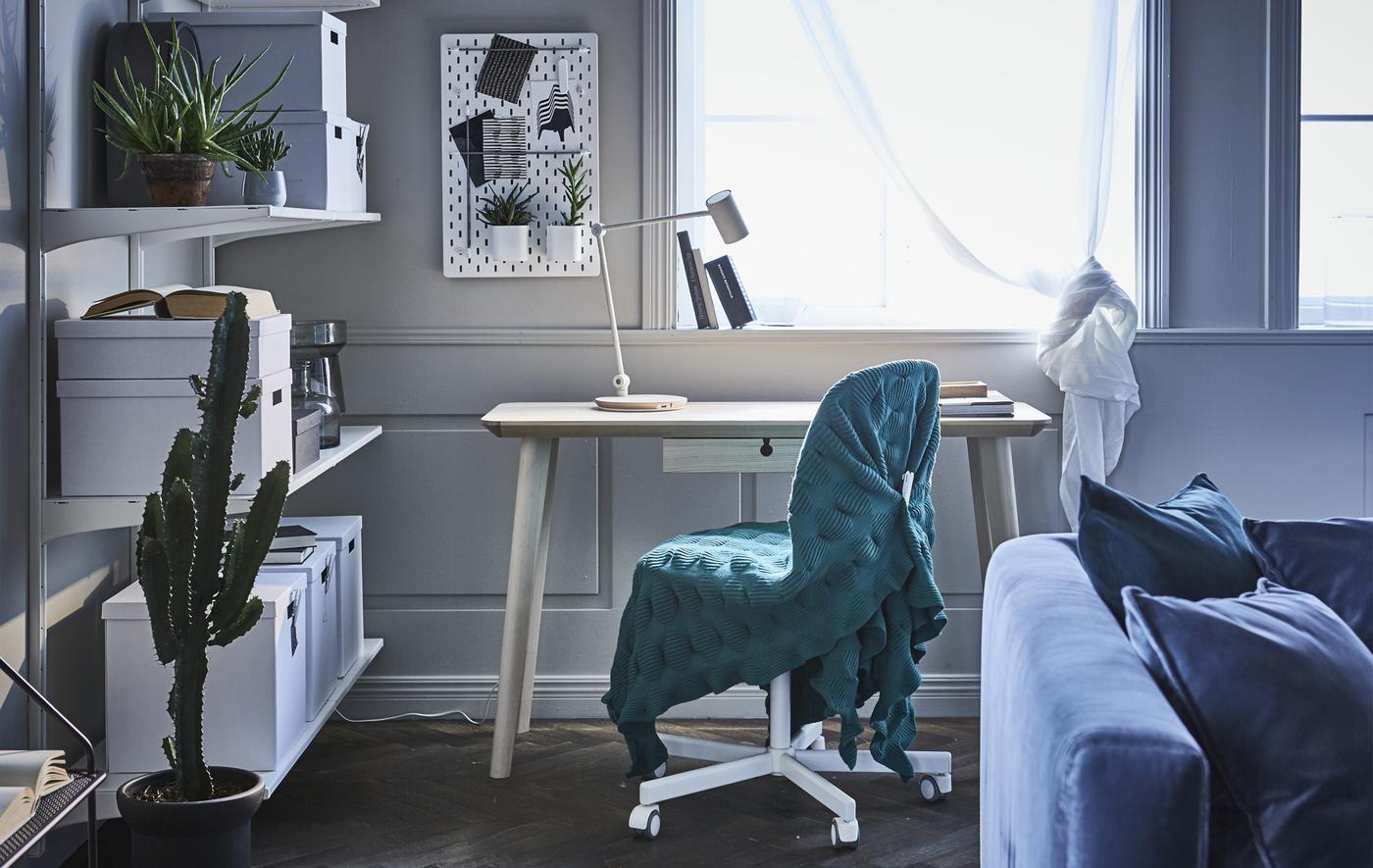 A home office workspace in a living room. Includes a desk, a chair draped in a throw, and open storage shelves