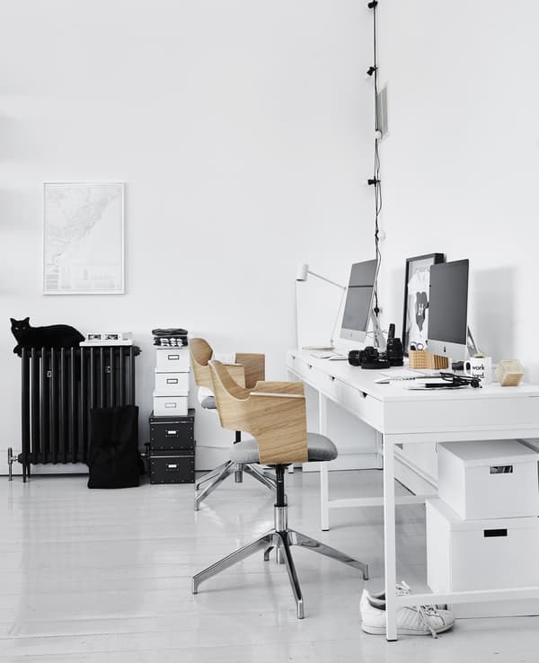 A home office workspace in the living room including two modern swivel chairs with wood backing and white work desks.