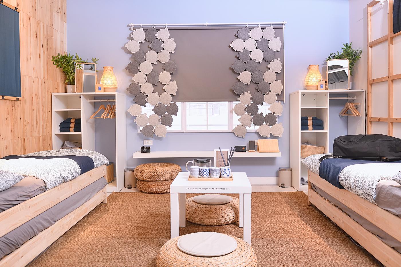 A hostel area featuring two single-sized beds, cabinets and wooden frames hung that is holding a towel.