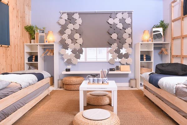 A hostel area featuring two single-sized beds, cabinets and wooden frames hung that is holding a towel.